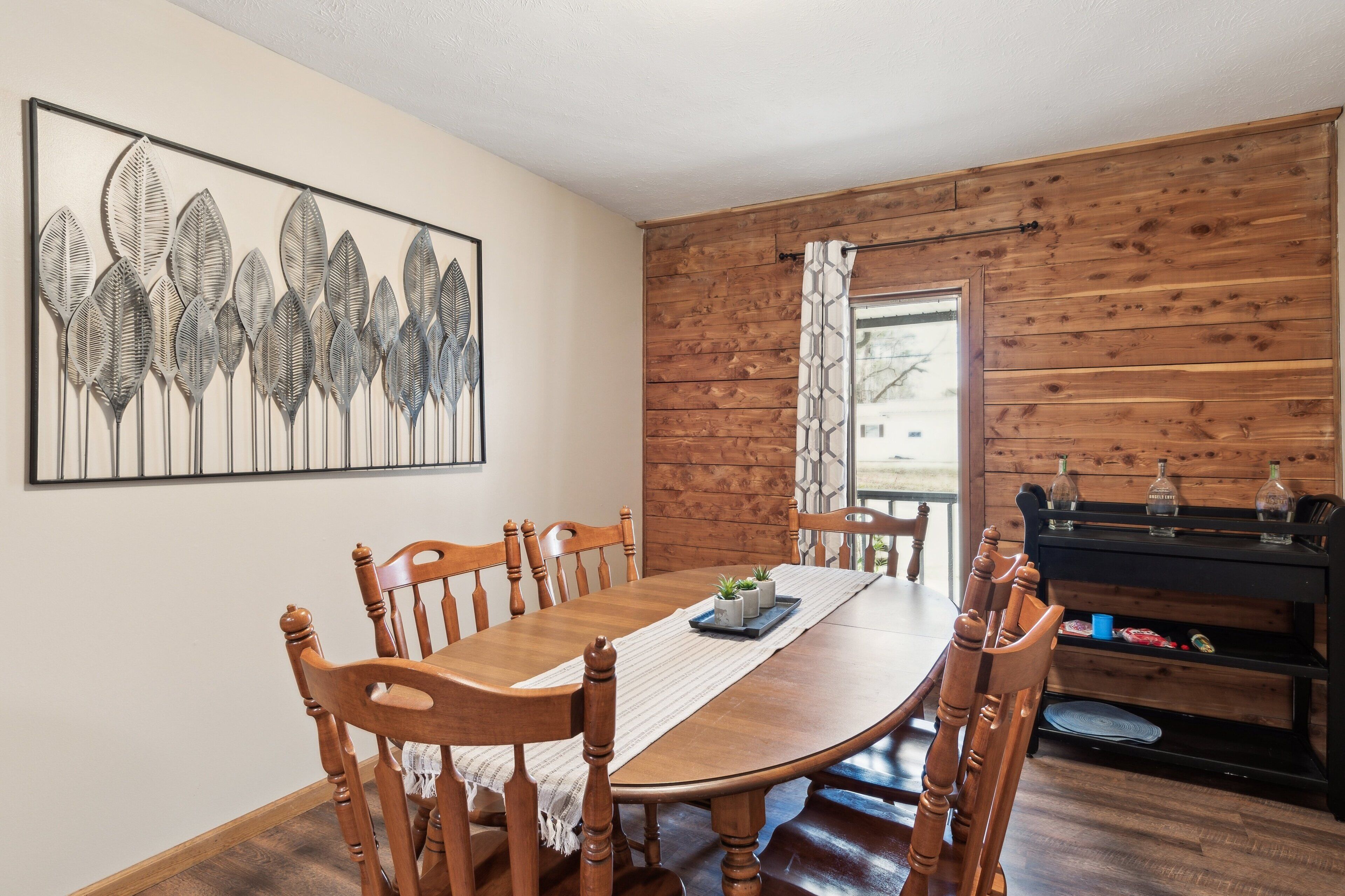 A dining area with a wooden table and chairs, a decorative wall piece, and a wooden panel wall.