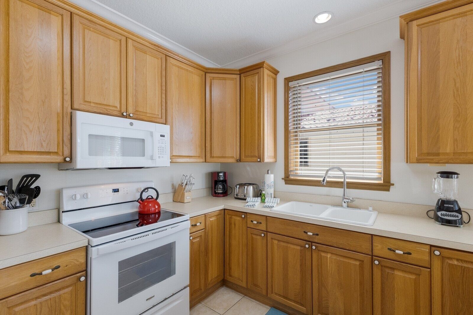 A kitchen with wooden cabinets, a microwave, stove, sink, and a window with blinds.