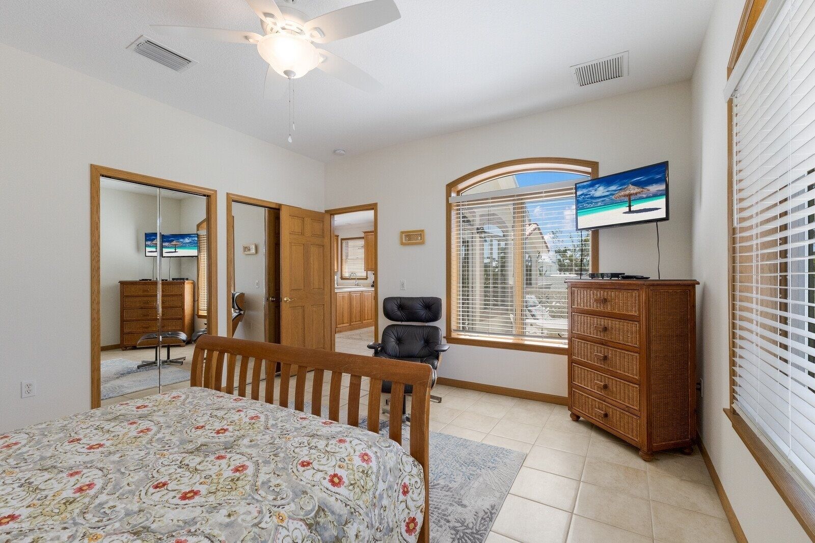 A bedroom with a bed, a desk, a chair, a dresser, a television, and a window with blinds.