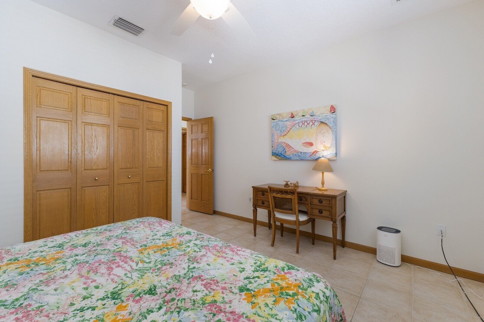 A bedroom with a bed, a desk, a chair, a lamp, and a wall-mounted painting.