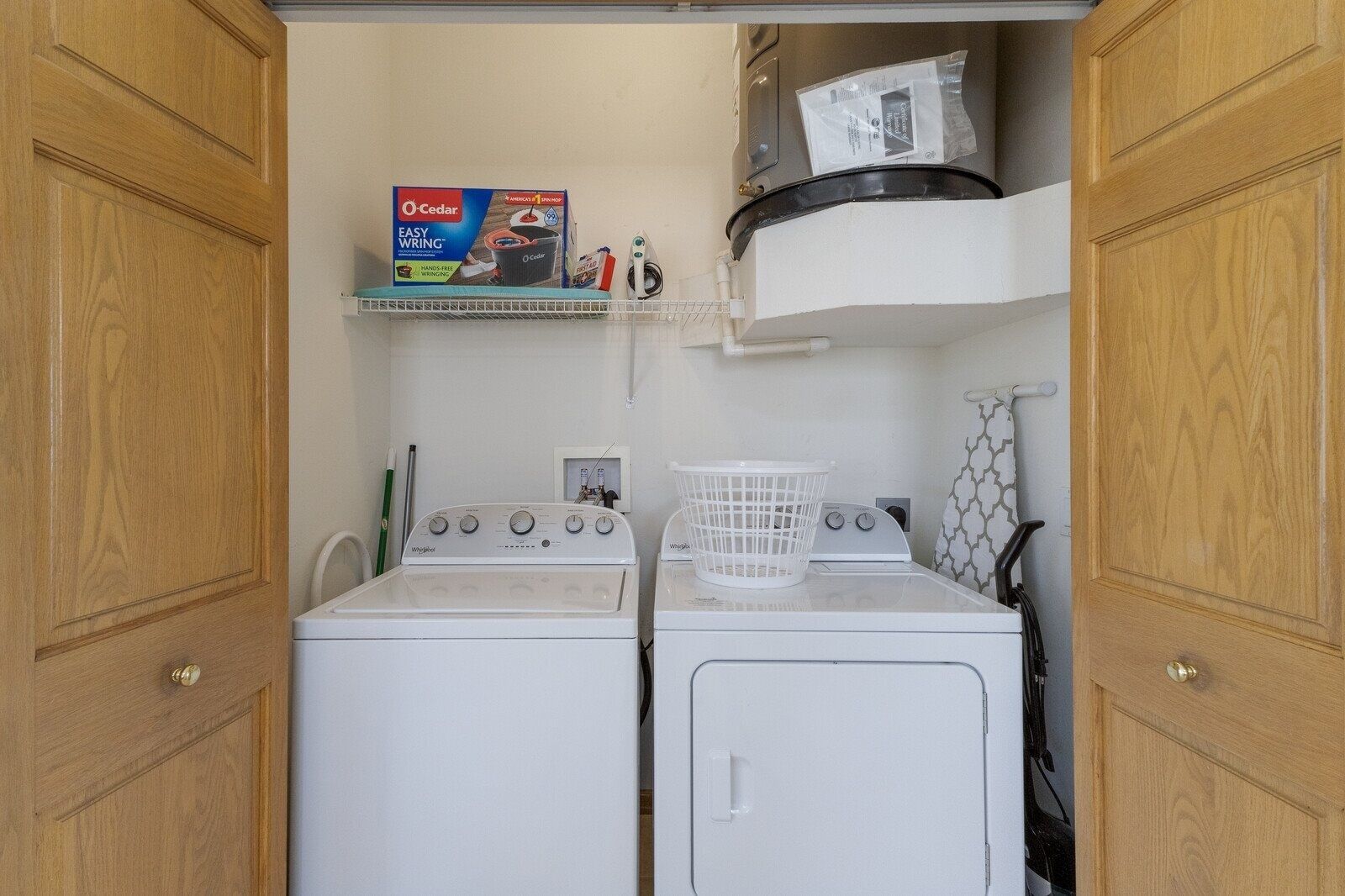 Une buanderie équipée de deux machines à laver à chargement frontal, d’un sèche-linge et d’une étagère sur laquelle se trouve une boîte de produits O’Cedar Easy Wrapping.