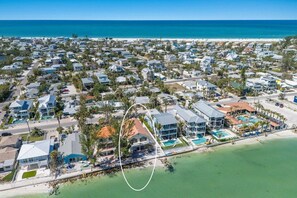 Ett flygbildsbild av ett bostadsområde vid kusten med hus, en strand och ett stort hotell med pool och direkt tillgång till stranden.