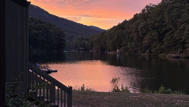 Une vue sur le lac, avec une terrasse en bois donnant accès à un quai, le tout entouré de collines boisées.