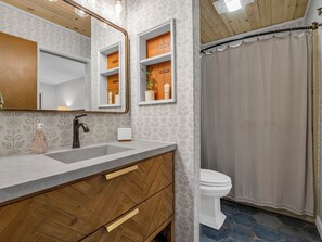 A bathroom with a wooden vanity, a large mirror, a sink, and a toilet. - Stylish waterfront 2 bedroom condo in Rumbling Bald at Lake Lure (Lake Lure)