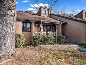 A two-story house with a wooden exterior, a front porch, and a flagpole with an American flag. - Stylish waterfront 2 bedroom condo in Rumbling Bald at Lake Lure (Lake Lure)