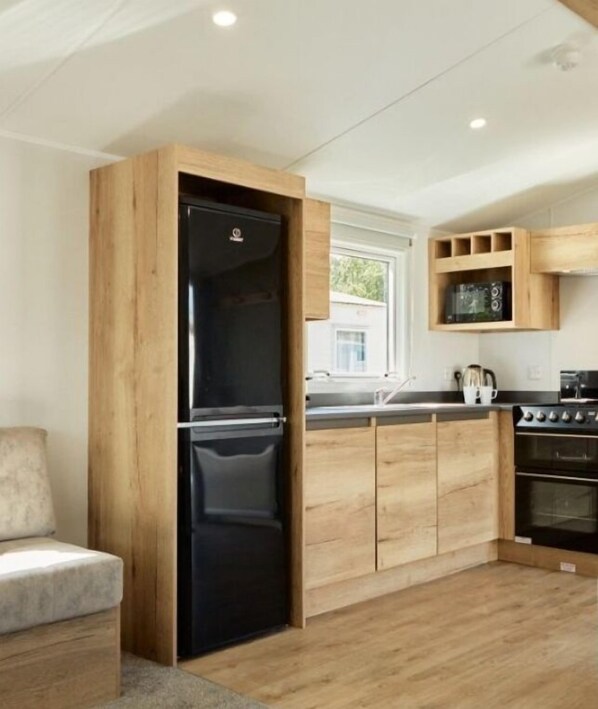A modern kitchen with wooden cabinets, a black refrigerator, a microwave, and a stove.