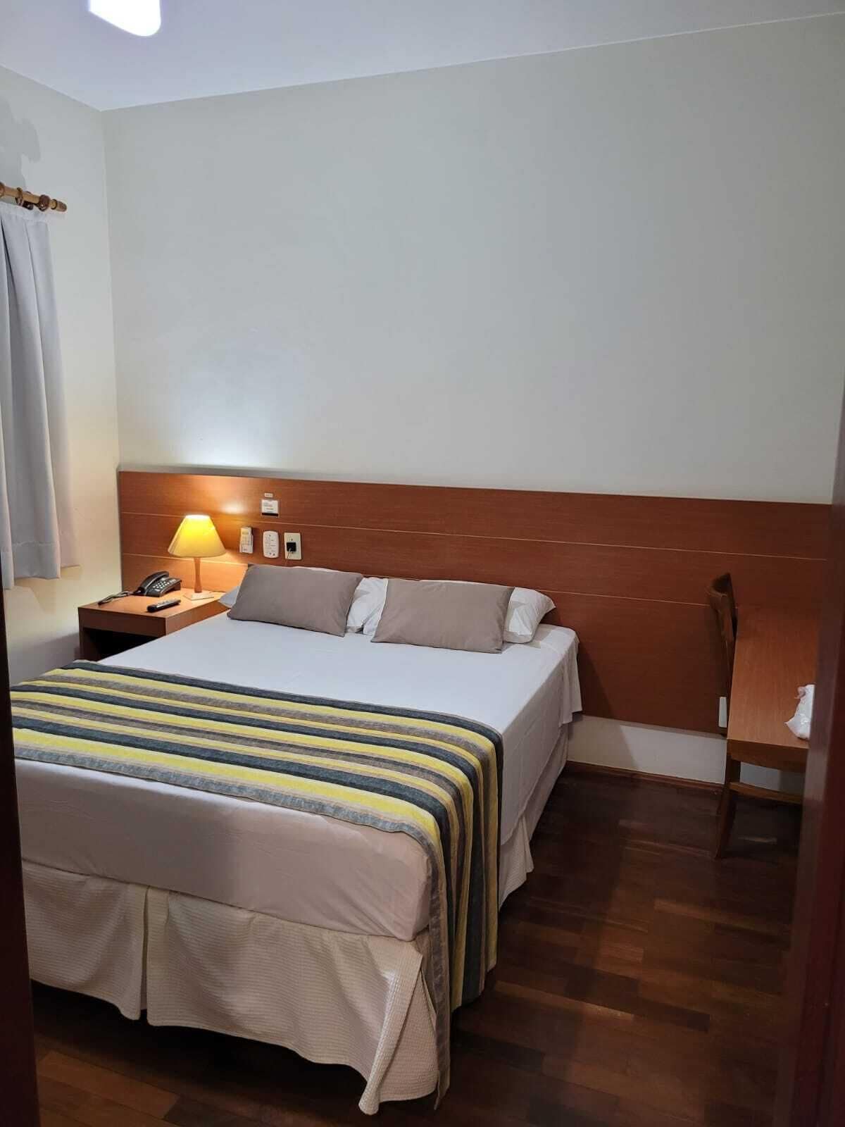 Une chambre d’hôtel avec un lit, une table de chevet, une lampe et une petite table en bois.