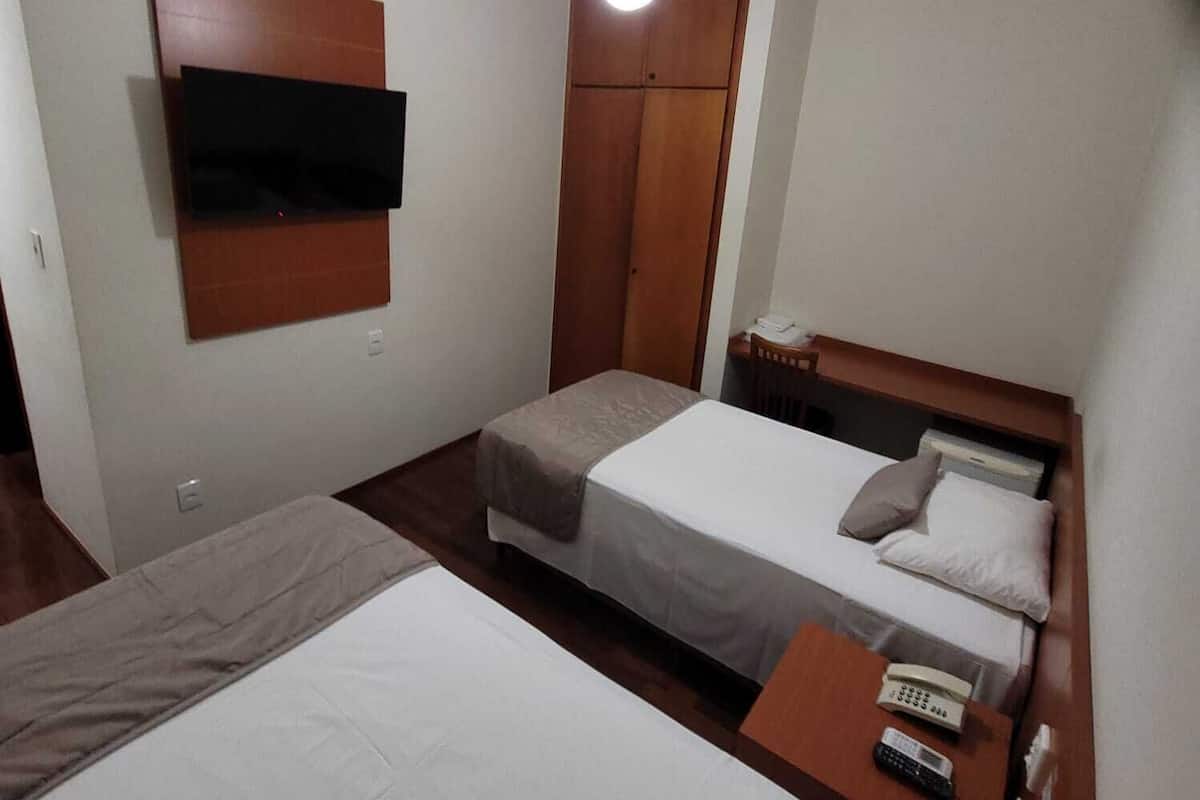 Une chambre d’hôtel avec deux lits simples, une armoire en bois, un téléviseur à écran plat fixé au mur et une table de chevet avec un téléphone et des télécommandes.
