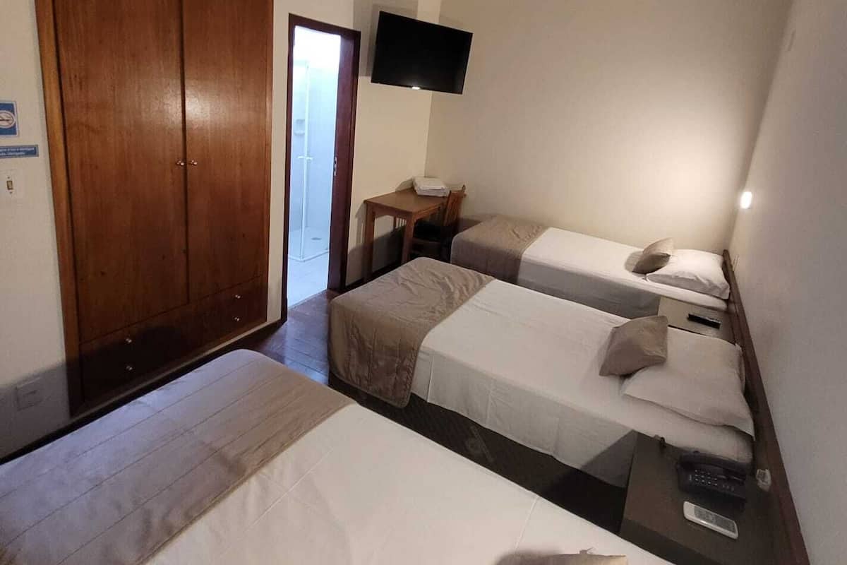 Une chambre d’hôtel avec deux lits simples, une armoire en bois, une petite table avec une chaise et un téléviseur fixé au mur.