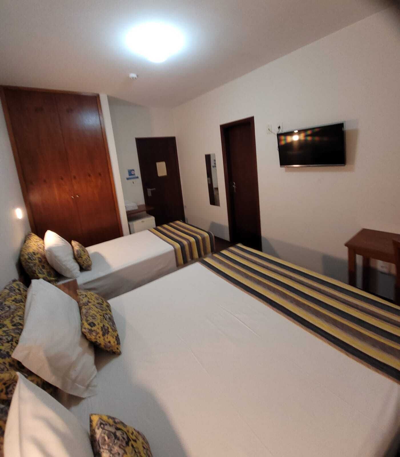 Een hotelkamer met twee bedden, een houten kledingkast, een televisie en een kleine tafel.