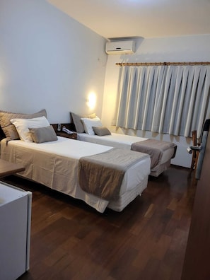 Une chambre d’hôtel avec deux lits, une table de chevet, une lampe, un appareil de climatisation et une fenêtre avec des rideaux.