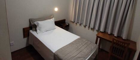 A hotel room with a bed, a nightstand, a desk, and a ceiling fan.