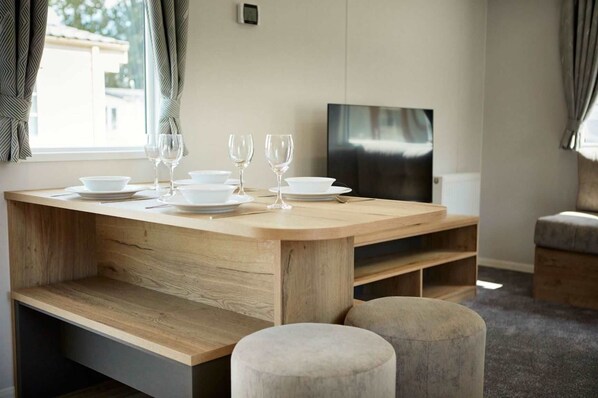 Un comedor moderno con una mesa de madera preparada para cuatro personas, un televisor de pantalla plana y una zona de estar acogedora.