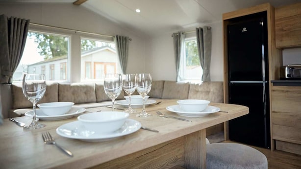 Un coin repas avec une table en bois dressée pour quatre personnes, comprenant des verres à vin, des assiettes et des couverts.