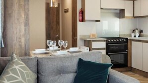 A modern kitchen with wooden beams, a dining area with a grey sofa, and a dining table set for four.