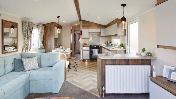 A modern living room with a light blue sofa, wooden coffee table, and a kitchen area with white cabinets and a wooden countertop.