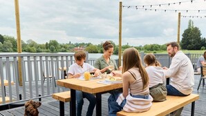 A group of people dining at an outdoor table with a view of a lake and trees in the background. - Billing Aquadrome Silver 3 Bed Caravan HW97 (Northampton)