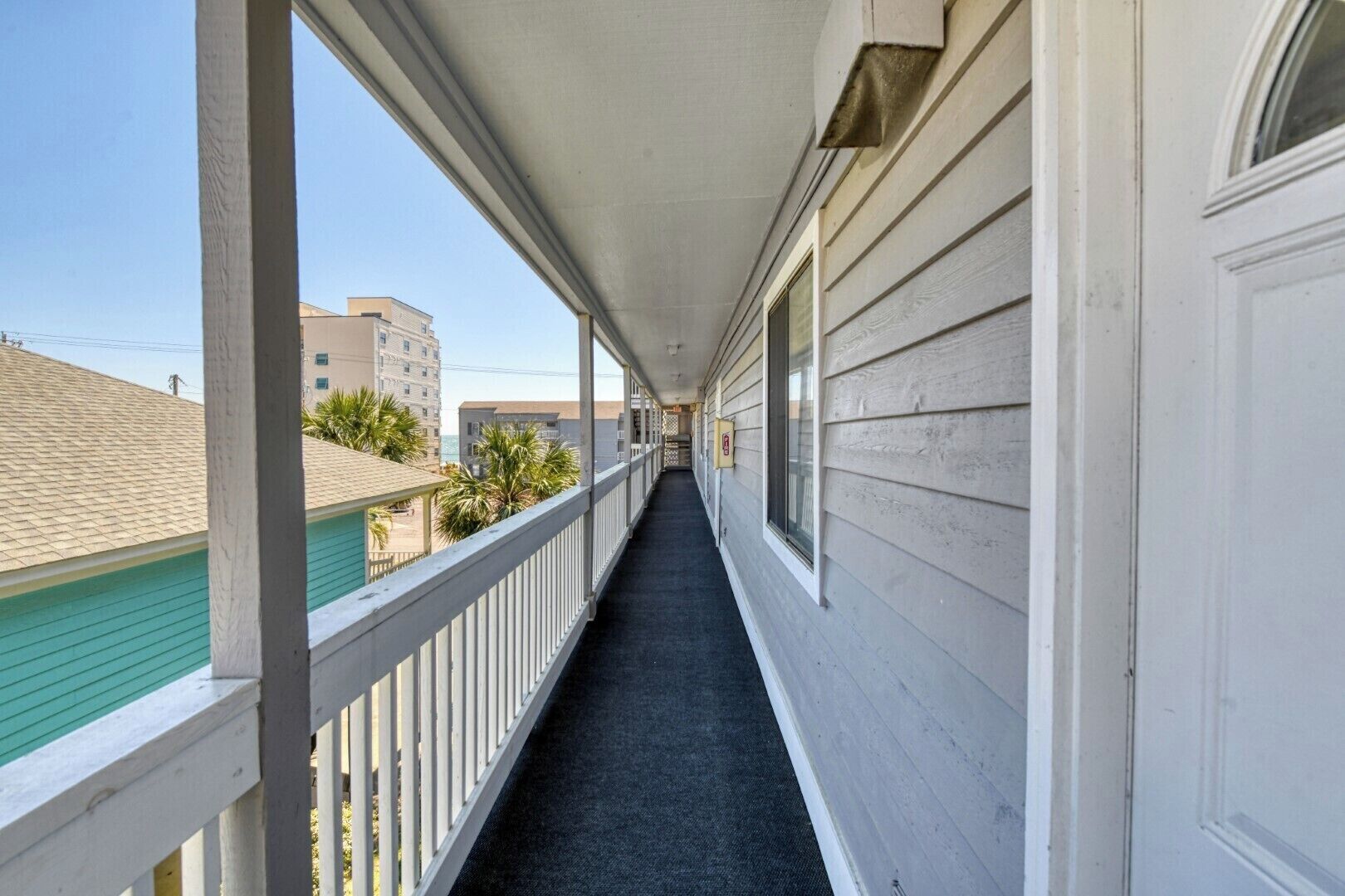 Varanda coberta com carpete preto, grades brancas e vista para edifícios vizinhos.