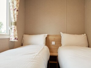 A hotel room with two beds, a wooden headboard, and a window with floral curtains.