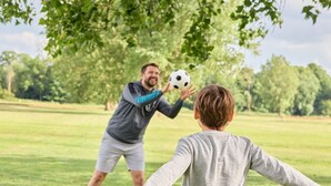 Eine Person spielt mit einer anderen Person Fußball in einem Park.