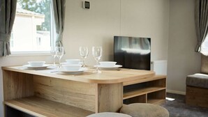 A modern dining area with a wooden table set for four, a flat-screen TV, and a cozy seating arrangement.