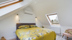 A bedroom with a sloped ceiling, a bed with floral bedding, a chair, and a window. - A tranquil farm stay in the Weald of Kent, 50mins from central London via PT. (Great Chart)
