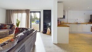 A modern living room with a sofa and a dining area with a kitchen in the background. - A tranquil farm stay in the Weald of Kent, 50mins from central London via PT. (Great Chart)