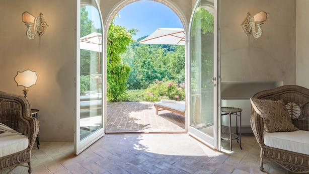 An open patio with a glass door leading to a lush garden, wicker furniture, and a white umbrella. - Col Di Casale - A breathtaking Umbrian villa in the green heart of Italy. (Pietralunga)