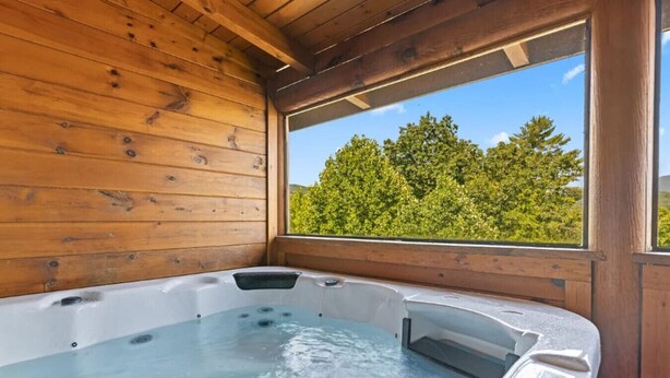 A wooden cabin with a hot tub and a window overlooking a forest. - Mama Bear Paw w/ private hot tub, two pools (Pigeon Forge)