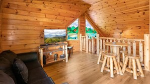 A cozy cabin interior with a wooden ceiling, a sofa, a TV, and a dining area with wooden stools. - Mama Bear Paw w/ private hot tub, two pools (Pigeon Forge)