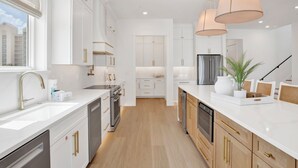 Una cocina moderna con armarios blancos, electrodomésticos de acero inoxidable e iluminación colgante.