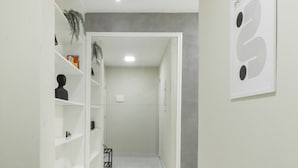A hallway with white walls, a marble floor, and a door leading to a room. Shelves with various items line one side, and a framed picture is on the wall. - Comfort in Ipanema 6 Minutes From the Beach J302 (Rio de Janeiro)