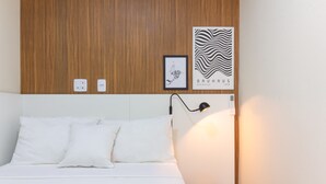 A neatly made bed with white bedding, a wooden headboard, a small bedside table with a lamp, and two framed artworks on the wall. - Comfort in Ipanema 6 Minutes From the Beach J302 (Rio de Janeiro)