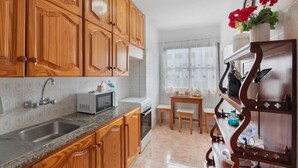 A kitchen with wooden cabinets, a microwave, a sink, a stove, and a dining area with a table and chairs. - 2 Bed Island Retreat-sleeps 4-5 Min Walk To Beach (Santa Cruz de la Palma)