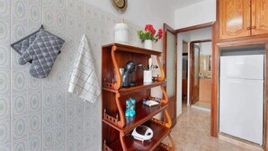Une cuisine avec des carreaux décoratifs, une étagère en bois où sont rangés les ustensiles de cuisine, une bouilloire et un réfrigérateur.