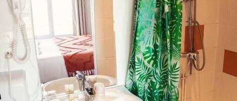 Un baño con un lavabo blanco, un espejo, una ducha con cortina estampada con motivos de hojas verdes y un teléfono en la pared.