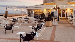 An outdoor seating area with tables and chairs, a building with a sign reading "LA COTE REVEE," and a view of the beach in the background. - La Côte Révéé (Leucate)