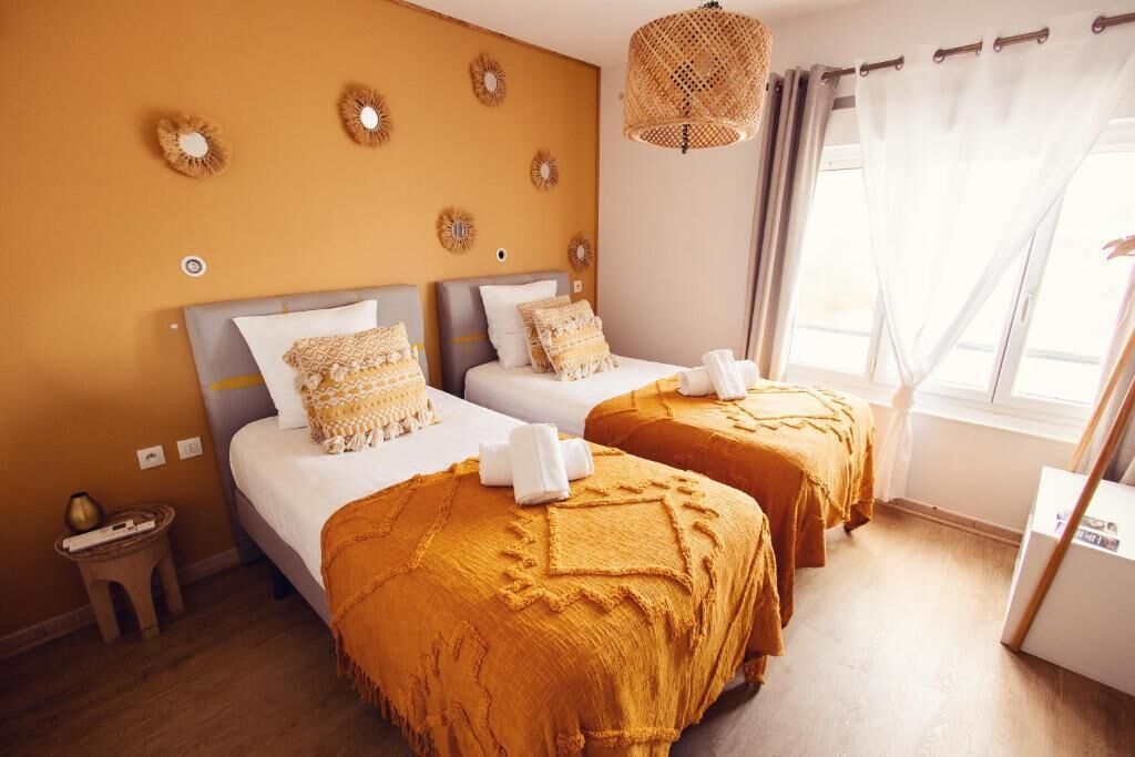 A room with two beds, each with a headboard and pillows, a small table, and a hanging light fixture.