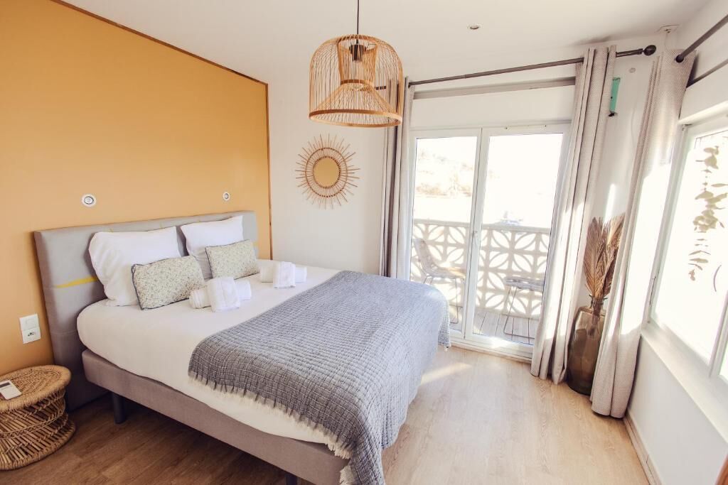 A bedroom with a bed, a hanging light fixture, a sun decoration, and a view of the outside.