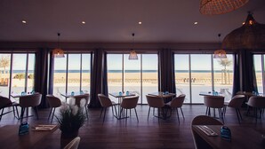 A restaurant with large windows offering a view of the beach. Tables and chairs are arranged for dining. - La Côte Révéé (Leucate)