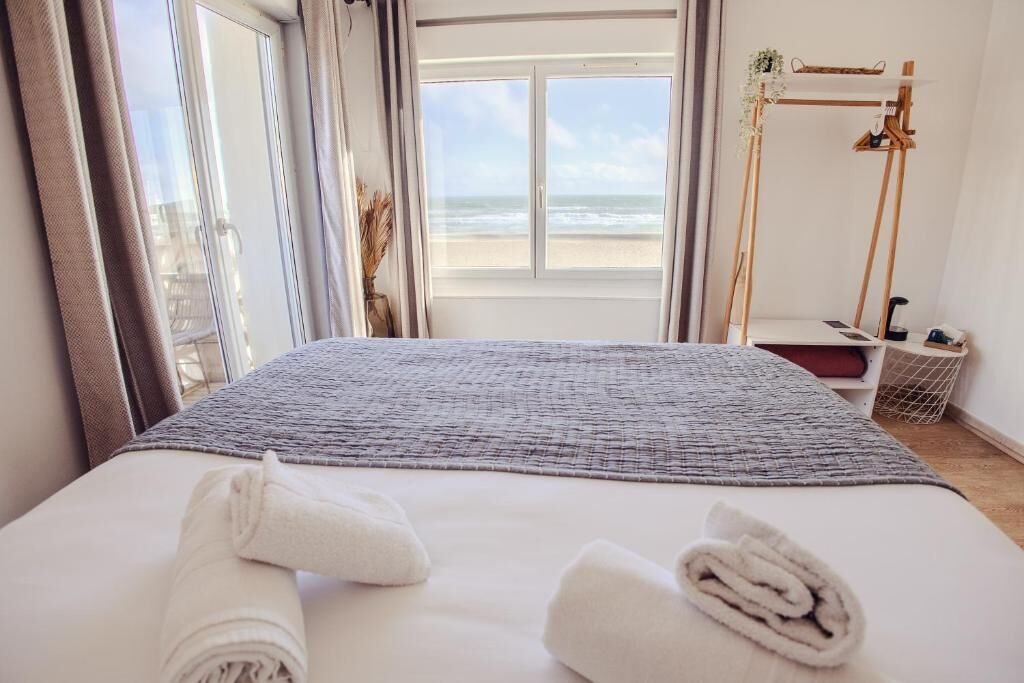 A hotel room with a bed, a view of the beach, and a wooden stand with a plant.