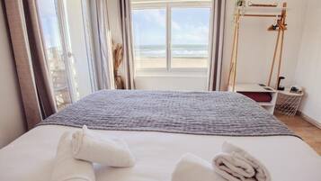 A hotel room with a bed, a view of the beach, and a wooden stand with a plant.