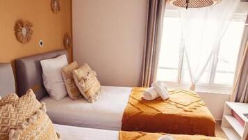 A hotel room with two beds, a large window with curtains, a woven light fixture, and decorative wall mirrors.