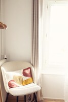 Rincón de una habitación con una silla blanca, una pared blanca y una ventana con cortinas.