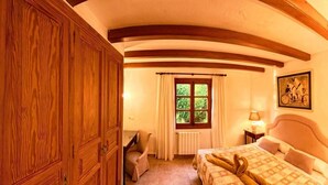 Ett mysigt sovrum med en stor trägarderob, en säng med ett mönstrat överkast, en stol, ett fönster med gardiner och en vägglampa.