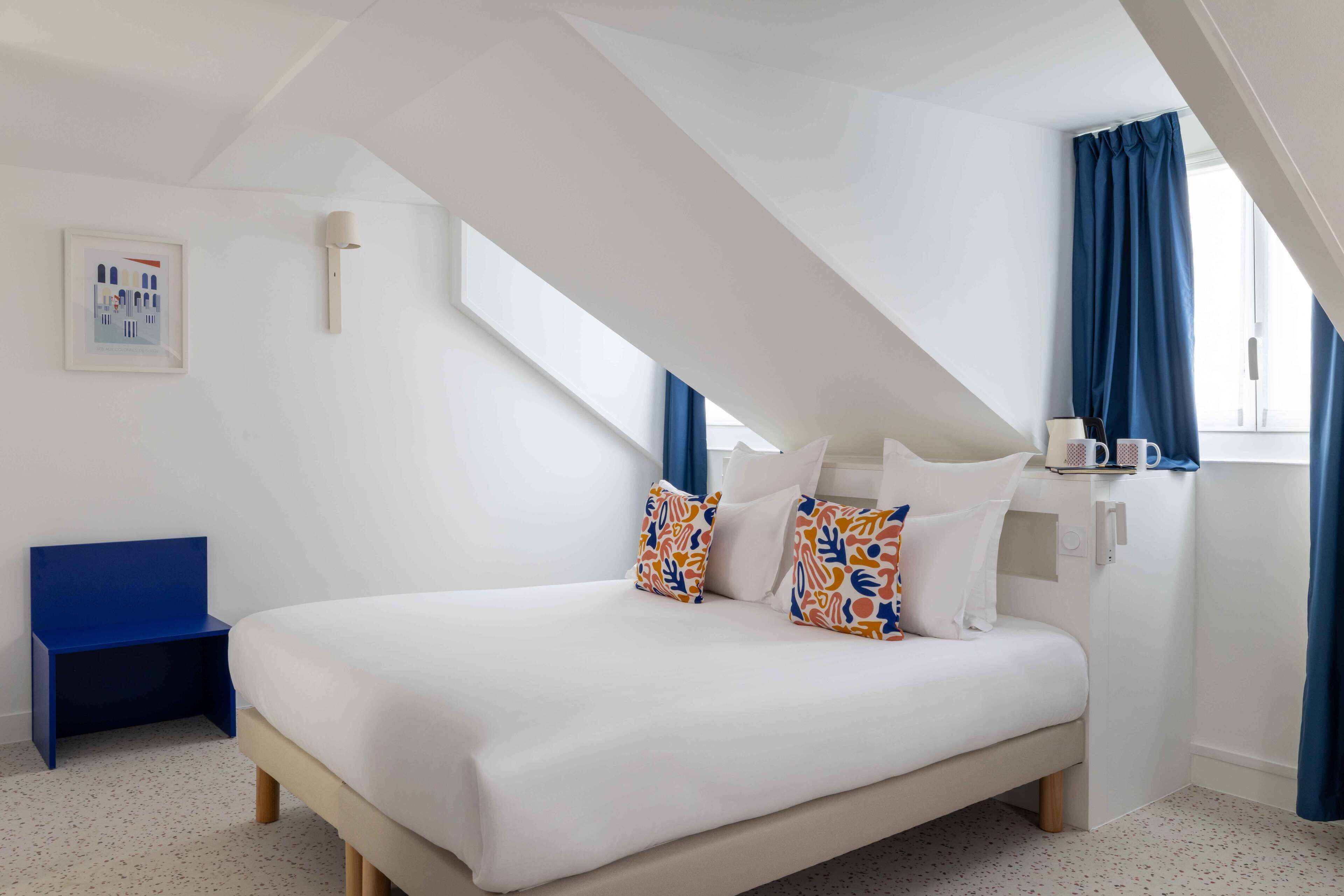 A bedroom with a bed, a blue chair, a framed picture, and a window with curtains.