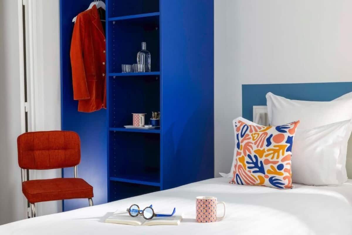A room with a bed, a red chair, a blue bookshelf, and a patterned pillow.