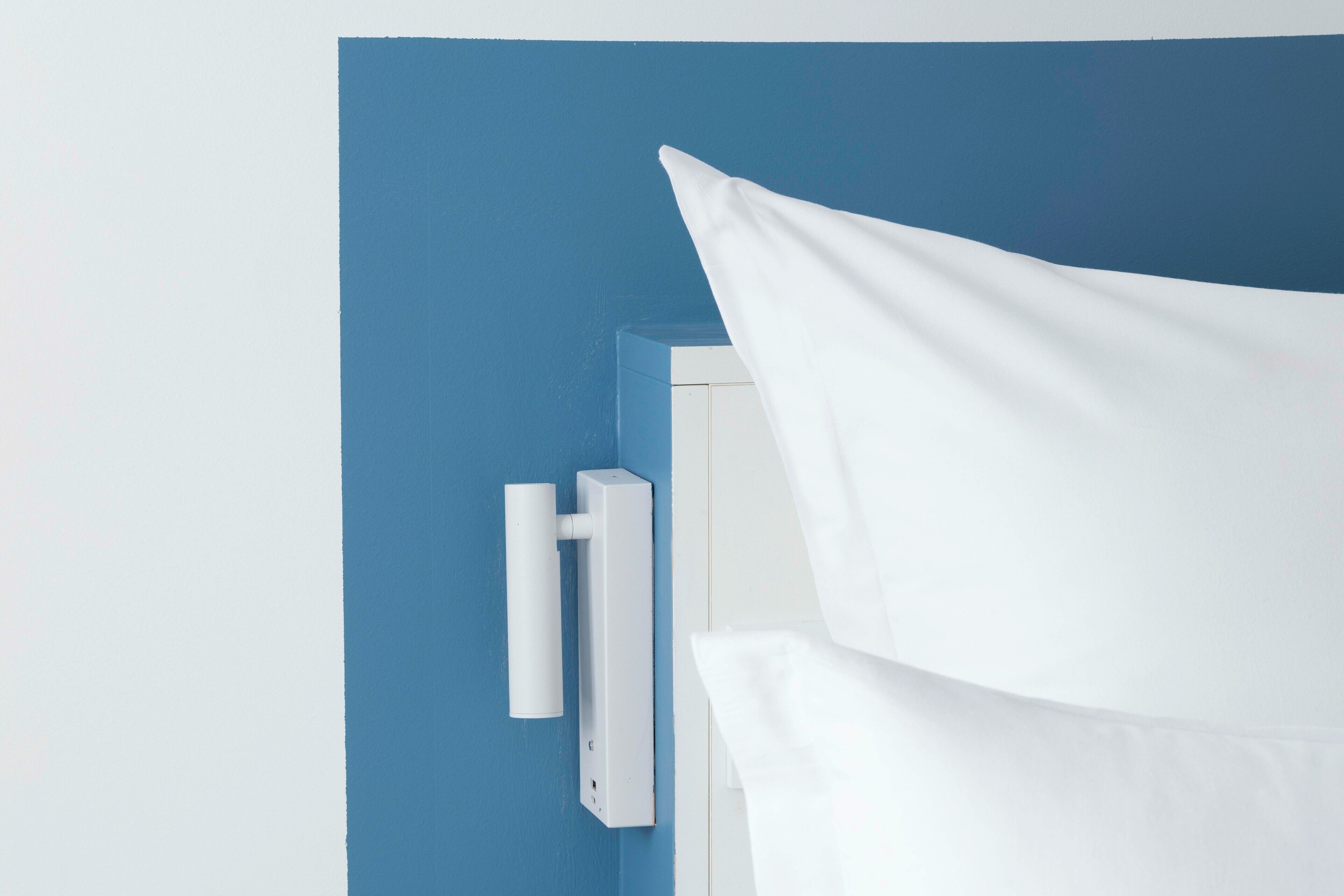 A white curtain partially drawn on a blue wall, a white door, and a white wall-mounted device.