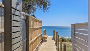 A wooden pathway leading to a beach with a wooden fence on one side and a white fence on the other.