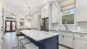 A modern kitchen with a large island, white cabinetry, stainless steel appliances, and a view to the outdoors.